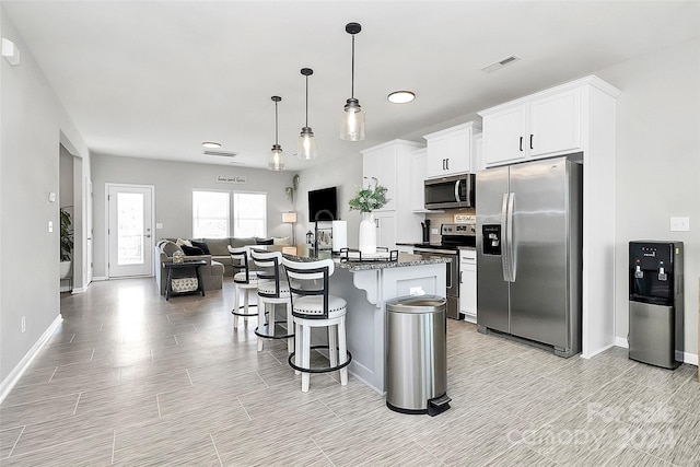 kitchen with white cabinets, decorative light fixtures, stainless steel appliances, an island with sink, and a breakfast bar area