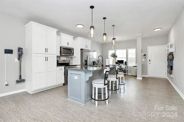 kitchen featuring decorative light fixtures, a center island with sink, appliances with stainless steel finishes, a breakfast bar, and white cabinetry