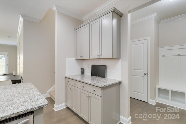 kitchen featuring crown molding, light stone counters, backsplash, and wood finished floors