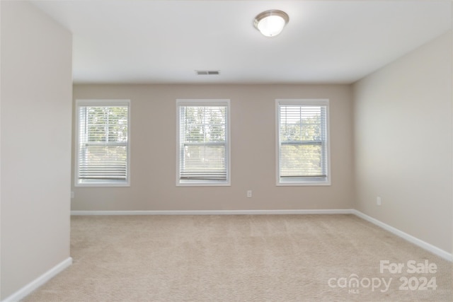 spare room with light carpet, a wealth of natural light, and visible vents