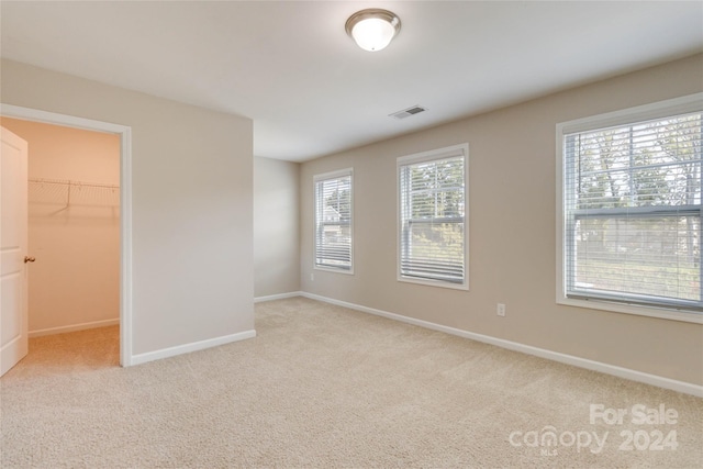 unfurnished bedroom featuring light carpet, visible vents, baseboards, a closet, and a walk in closet