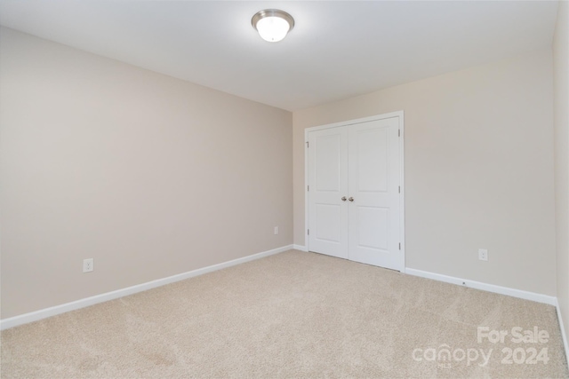 unfurnished bedroom with baseboards, a closet, and light colored carpet