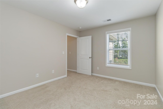 spare room featuring light colored carpet, visible vents, and baseboards