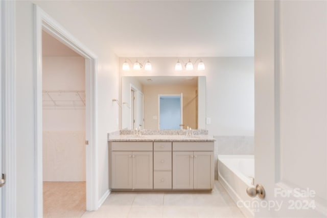 bathroom with double vanity, a bath, tile patterned floors, a spacious closet, and a sink