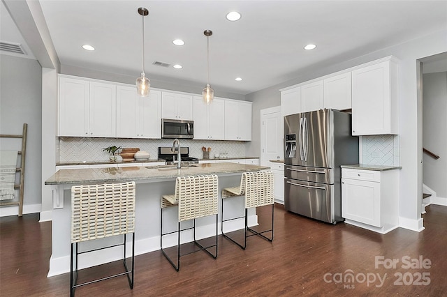 kitchen featuring a breakfast bar, white cabinetry, hanging light fixtures, stainless steel appliances, and an island with sink