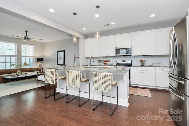 kitchen featuring appliances with stainless steel finishes, pendant lighting, an island with sink, sink, and white cabinets