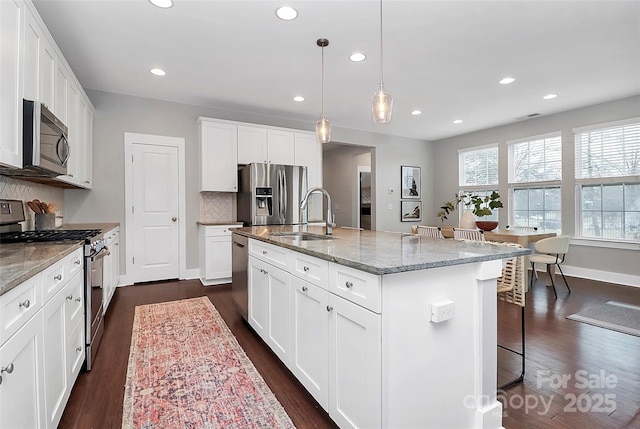 kitchen with appliances with stainless steel finishes, pendant lighting, white cabinetry, an island with sink, and sink