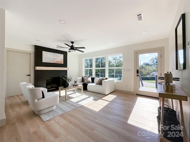 living room featuring a large fireplace, light hardwood / wood-style flooring, and ceiling fan