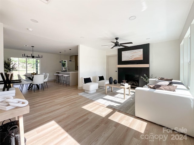 living room with ceiling fan with notable chandelier, a large fireplace, and light hardwood / wood-style floors