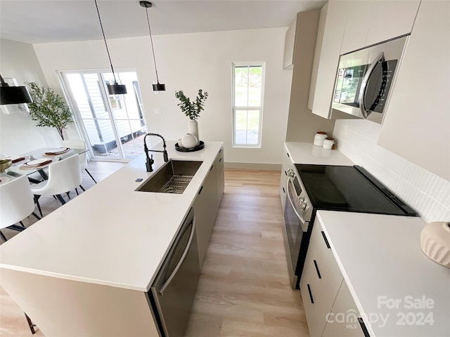 kitchen with appliances with stainless steel finishes, light hardwood / wood-style floors, pendant lighting, a kitchen island with sink, and sink