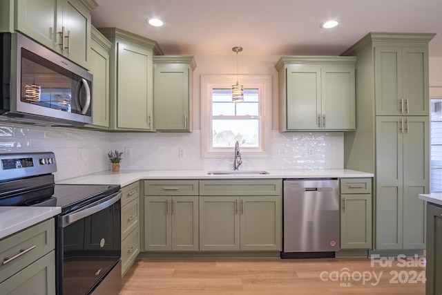 kitchen featuring stainless steel appliances, pendant lighting, decorative backsplash, sink, and light hardwood / wood-style floors