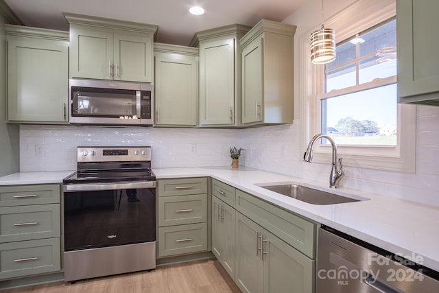 kitchen with light wood-type flooring, appliances with stainless steel finishes, hanging light fixtures, decorative backsplash, and sink