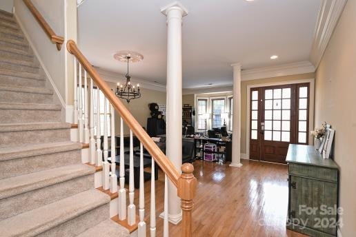 foyer with wood-type flooring, decorative columns, crown molding, and an inviting chandelier