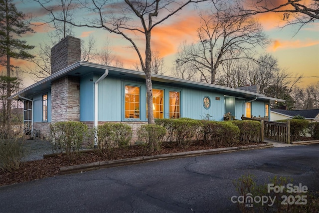 property exterior at dusk featuring stone siding and a chimney