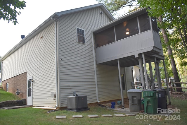 rear view of house featuring a lawn, a sunroom, and central AC