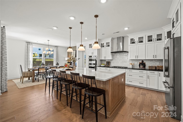 kitchen featuring pendant lighting, wall chimney exhaust hood, a center island with sink, appliances with stainless steel finishes, and dark hardwood / wood-style flooring