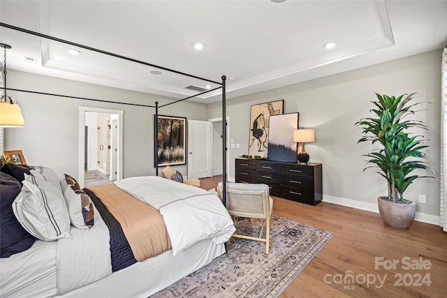 bedroom featuring a tray ceiling, light hardwood / wood-style floors, and ensuite bathroom