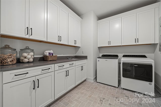 clothes washing area featuring sink, washing machine and clothes dryer, and cabinets