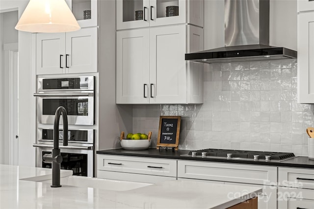 kitchen featuring wall chimney exhaust hood, backsplash, white cabinetry, stainless steel appliances, and dark stone countertops