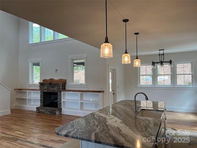 kitchen featuring sink, dark stone counters, decorative light fixtures, a fireplace, and hardwood / wood-style flooring