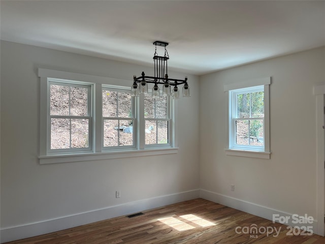 unfurnished dining area with wood-type flooring and a notable chandelier