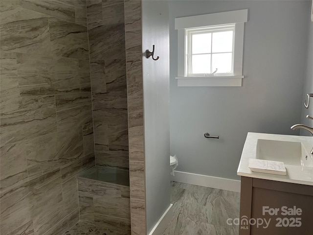 bathroom with a tile shower, vanity, and toilet