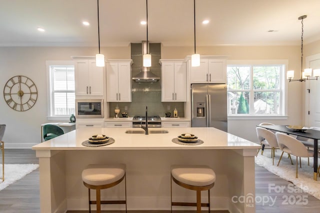 kitchen featuring built in microwave, wall chimney exhaust hood, hanging light fixtures, stainless steel fridge with ice dispenser, and a center island with sink