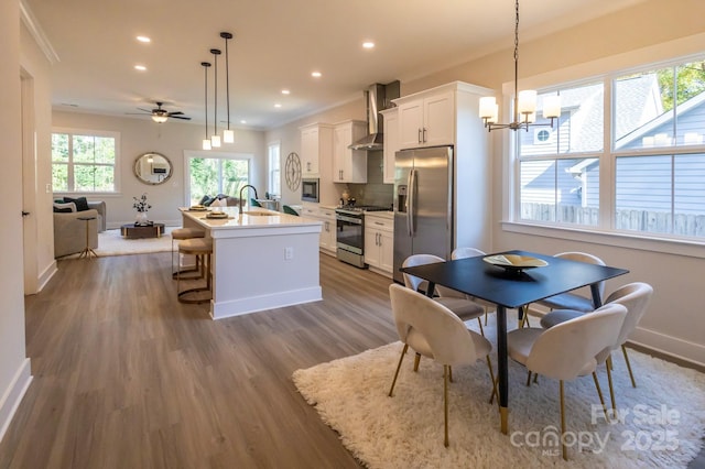 kitchen with a kitchen island with sink, wall chimney exhaust hood, decorative light fixtures, white cabinetry, and stainless steel appliances