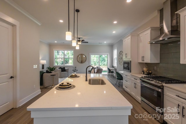 kitchen with wall chimney range hood, sink, appliances with stainless steel finishes, and an island with sink