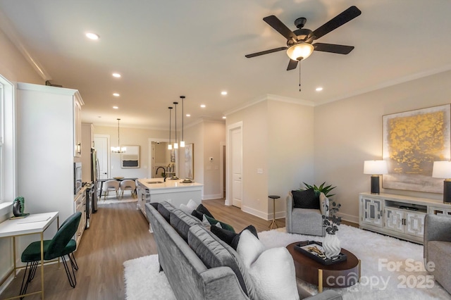 living room with crown molding, sink, light hardwood / wood-style floors, and ceiling fan with notable chandelier