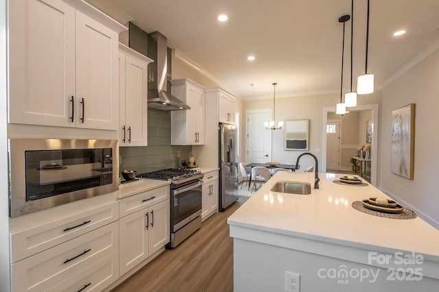 kitchen with pendant lighting, a kitchen island with sink, sink, wall chimney exhaust hood, and appliances with stainless steel finishes