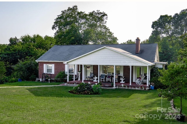 view of front facade with a front lawn, a porch, brick siding, and a chimney