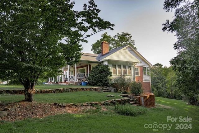 view of front of property with brick siding, a porch, a chimney, and a front yard