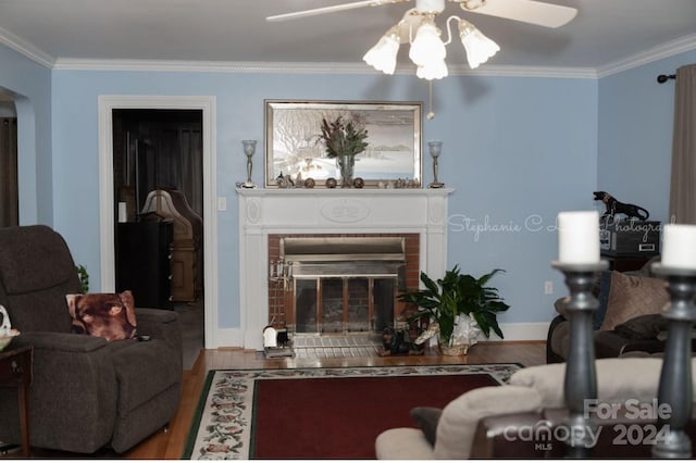 living room with crown molding, hardwood / wood-style flooring, a brick fireplace, and ceiling fan