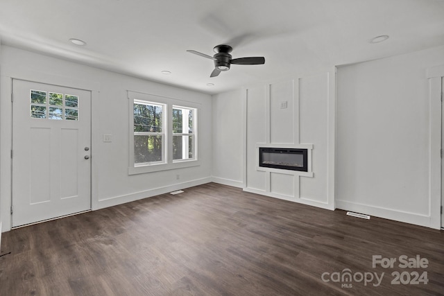 unfurnished living room with dark wood-style floors, baseboards, a ceiling fan, and a glass covered fireplace