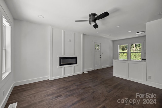 unfurnished living room featuring dark wood-style floors, a glass covered fireplace, visible vents, and baseboards