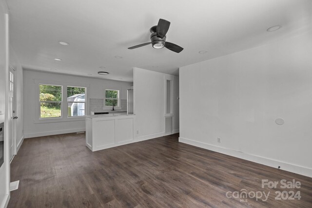 unfurnished living room with a ceiling fan, a sink, dark wood finished floors, and baseboards