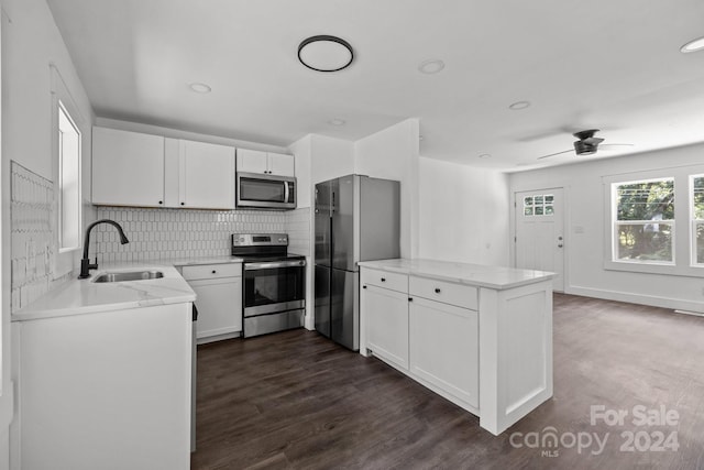 kitchen with stainless steel appliances, a peninsula, a sink, white cabinetry, and decorative backsplash