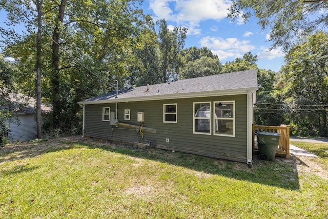 rear view of house with roof with shingles and a lawn