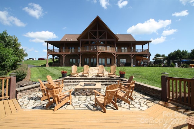 rear view of house with a balcony, a patio, a lawn, and an outdoor fire pit