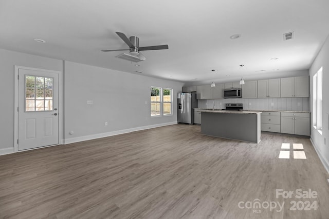 kitchen with gray cabinets, light wood-type flooring, tasteful backsplash, stainless steel appliances, and a kitchen island