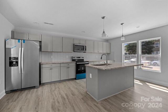 kitchen featuring a kitchen island with sink, stainless steel appliances, sink, light stone countertops, and light hardwood / wood-style floors