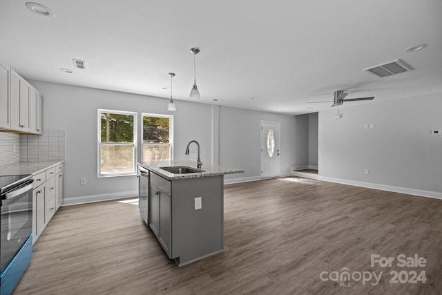 kitchen featuring a kitchen island with sink, light wood-type flooring, sink, hanging light fixtures, and appliances with stainless steel finishes