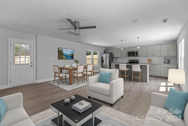 living room featuring ceiling fan, sink, and light wood-type flooring