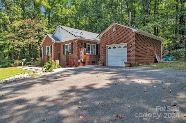 view of front of home featuring metal roof, an attached garage, brick siding, driveway, and a view of trees