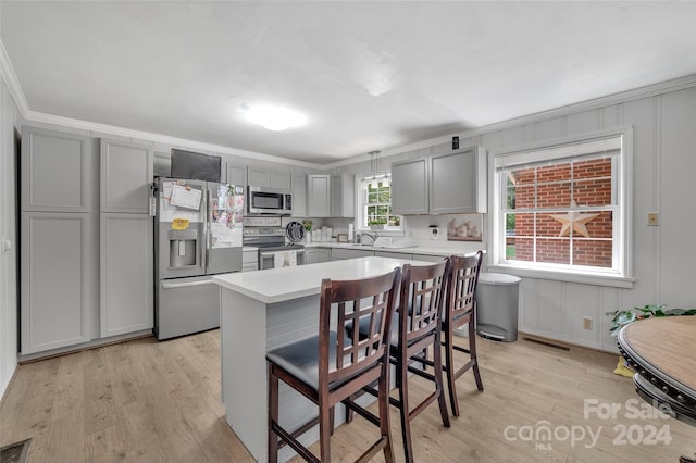 kitchen with light hardwood / wood-style flooring, appliances with stainless steel finishes, crown molding, a breakfast bar, and gray cabinets