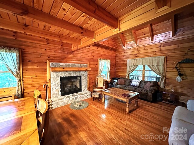 living room featuring beamed ceiling, wood walls, a stone fireplace, wooden ceiling, and hardwood / wood-style flooring