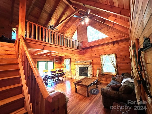 living room featuring wooden walls, ceiling fan, a stone fireplace, wood ceiling, and hardwood / wood-style flooring