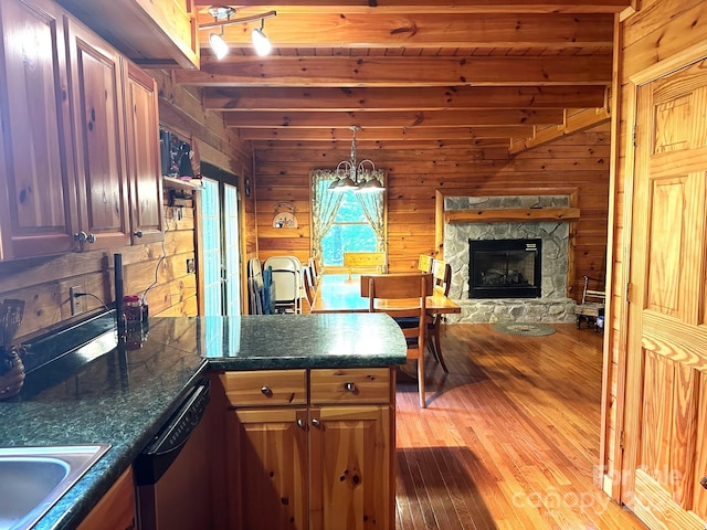 kitchen with a fireplace, light hardwood / wood-style flooring, wood walls, beam ceiling, and stainless steel dishwasher