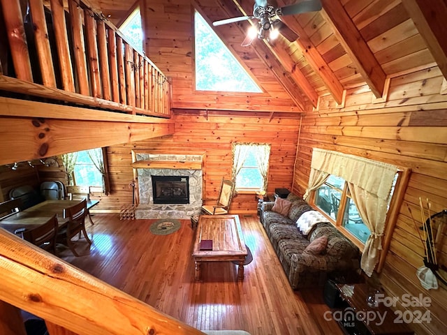 unfurnished living room featuring hardwood / wood-style flooring, a fireplace, ceiling fan, wood walls, and high vaulted ceiling